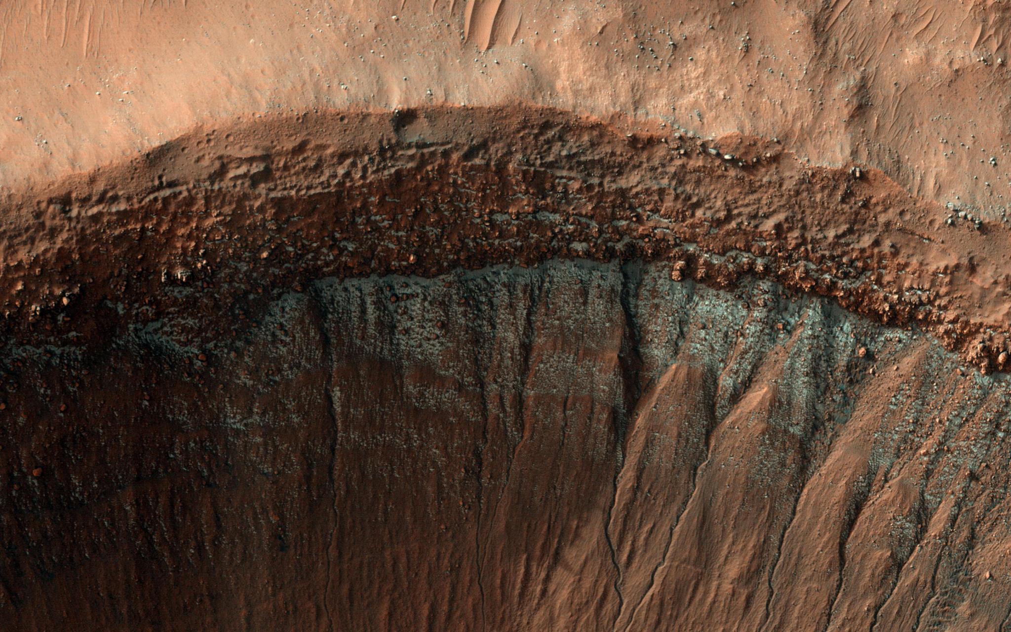 The HiRISE camera captured this image of the edge of a crater in the middle of winter. The south-facing slope of the crater, which receives less sunlight, has formed patchy, bright frost, seen in blue in this enhanced-color image.