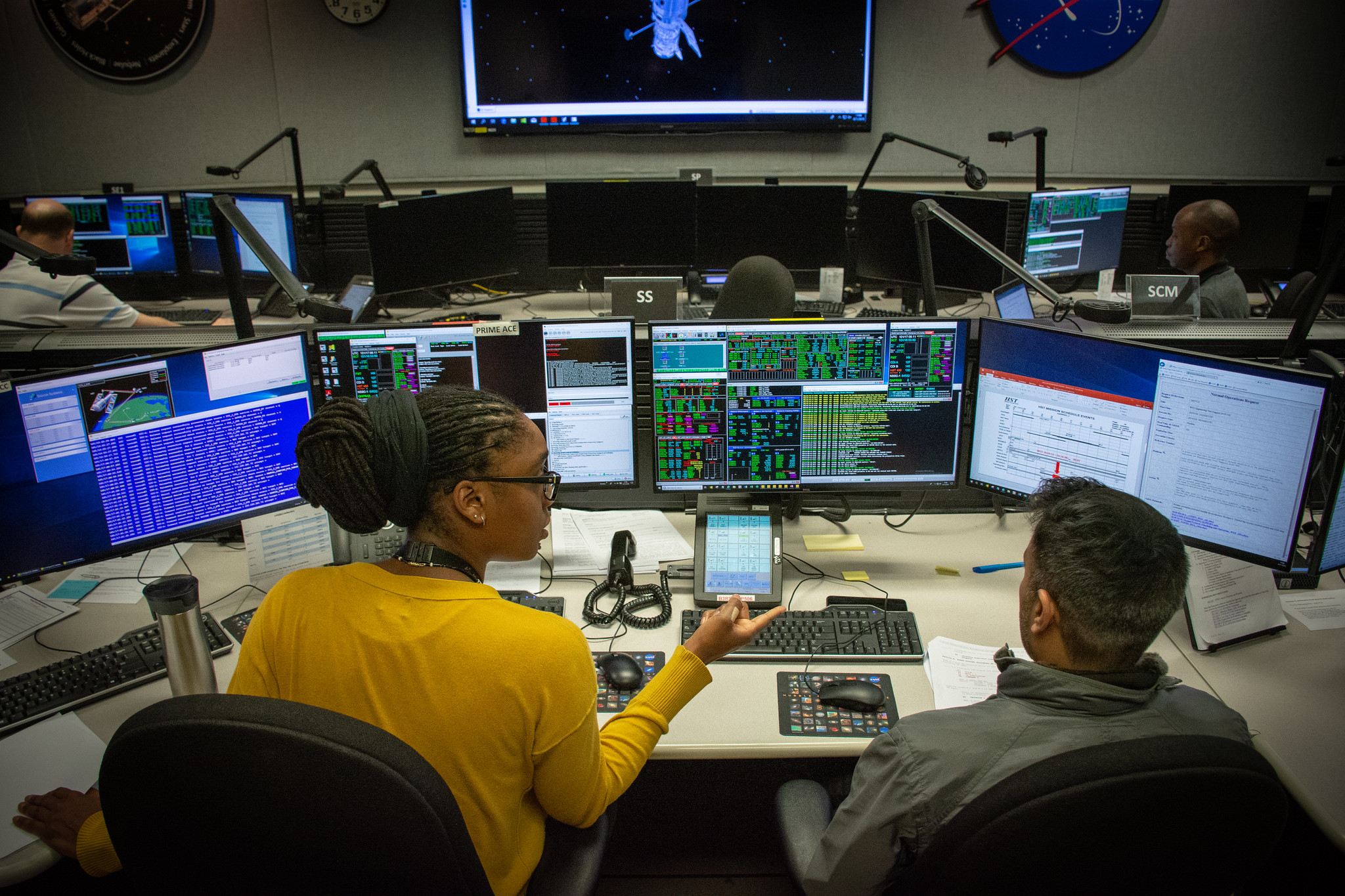 Two employees sit in front of a bank of computer screens in the Mission Operations Room for the Hubble Space Telescope at NASA's Goddard Space Flight Center in Maryland.