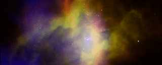 A colorful composite image of a large gas cloud flecked with white dots. RCW 36 is a mustard yellow, burnt orange, royal blue, and violet cloud.