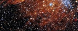 This cluster in the Large Magellanic Cloud is surrounded by a crimson nebula of gas and dust extending across the image, where new stars may someday form. Orange and red in this image indicates visible and near-infrared light, respectively.