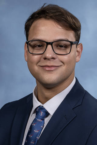 A portrait of a young man in glasses in a suit with a blue tie.