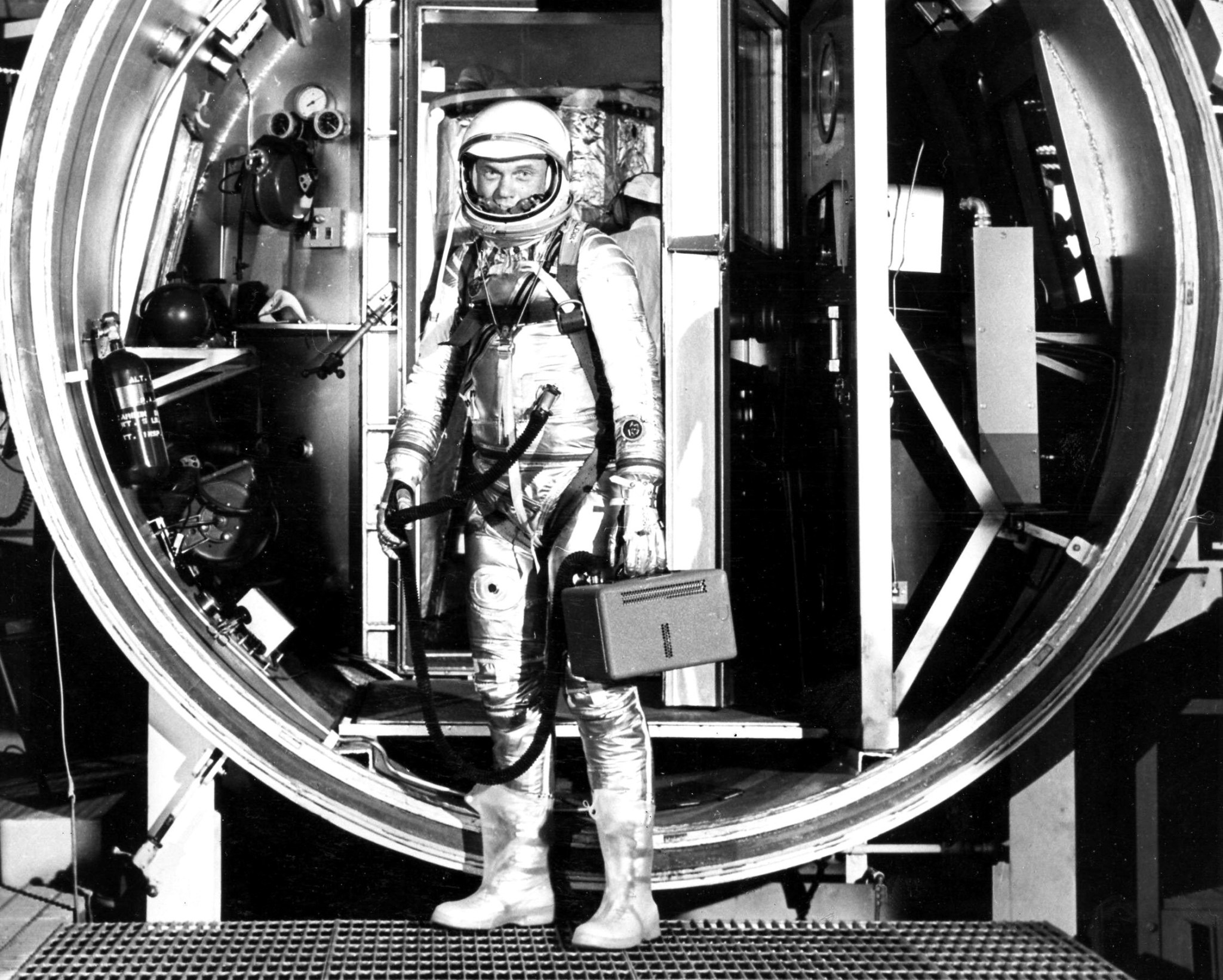 Astronaut John Glenn, suited with hose to suit ventilation unit attached, is seen preparing to board his Mercury spacecraft inside the Hangar S altitude chamber. 