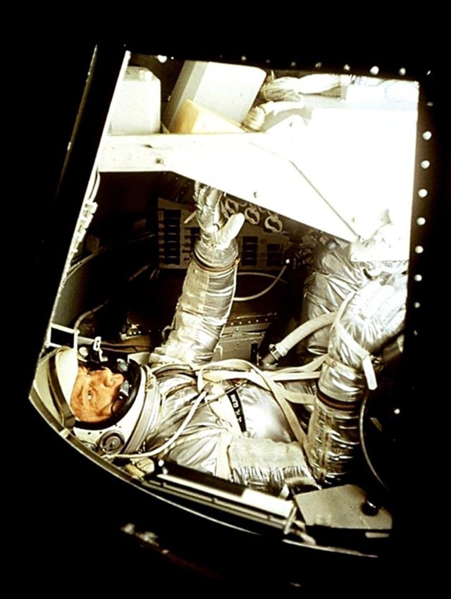 John Glenn, suited in his silver space suit, works in the procedures trainer for the Mercury-Atlas 6 mission.