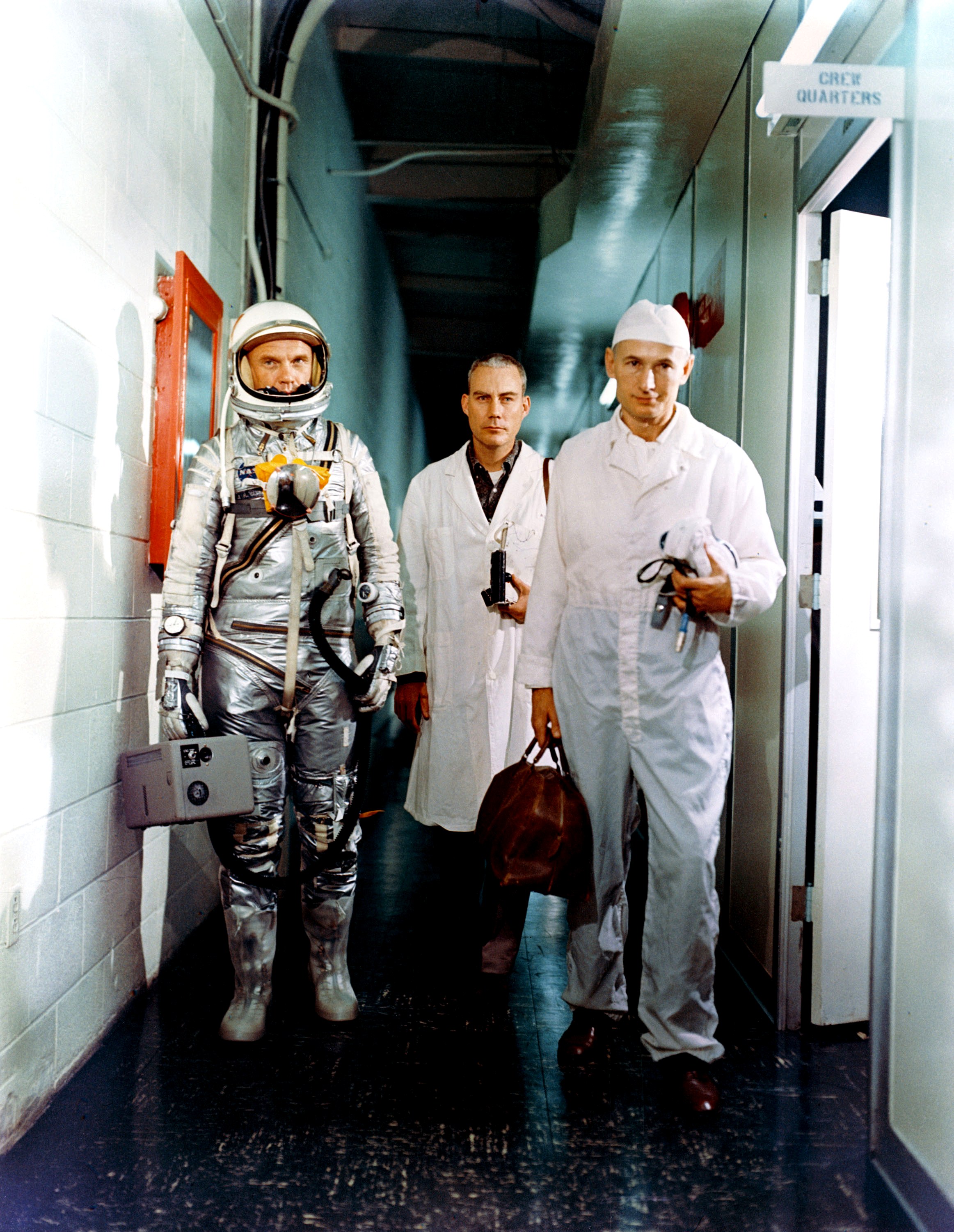 Astronaut John H. Glenn Jr. (left), Dr. William Douglas, astronauts flight surgeon, and equipment specialist Joe Schmitt walk down a hall as they leave crew quarters prior to Mercury-Atlas 6 (MA-6) mission.