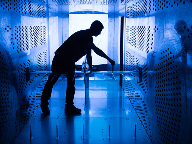 man silhouetted in a blue lit wind tunnel holding an aircraft model for setup