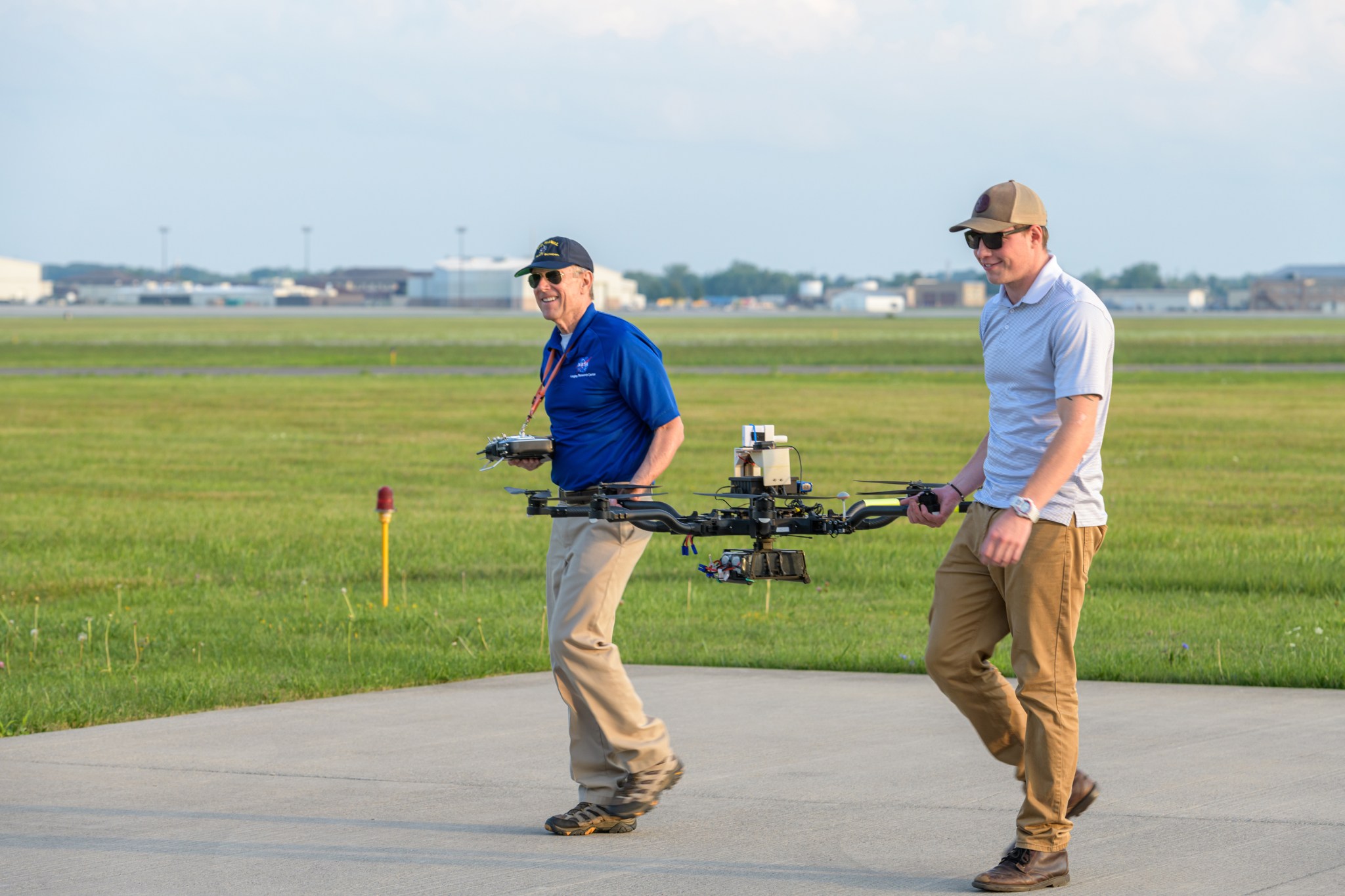 Dois funcionários da NASA segurando o drone em cada extremidade.