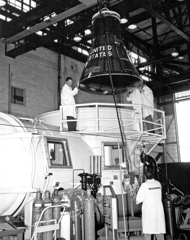 A Mercury spacecraft is moved into the altitude chamber inside Hangar S with the help of McDonnell technicians.