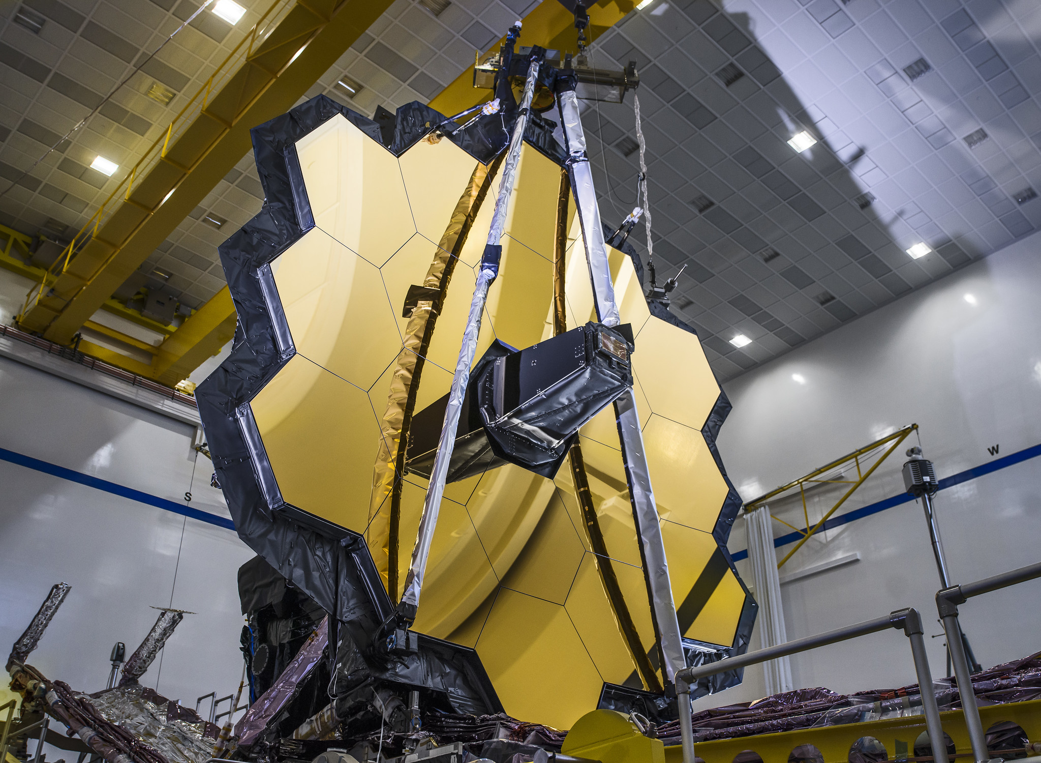 gold-hued hexagonal primary mirror of Webb telescope, photographed inside a clean room