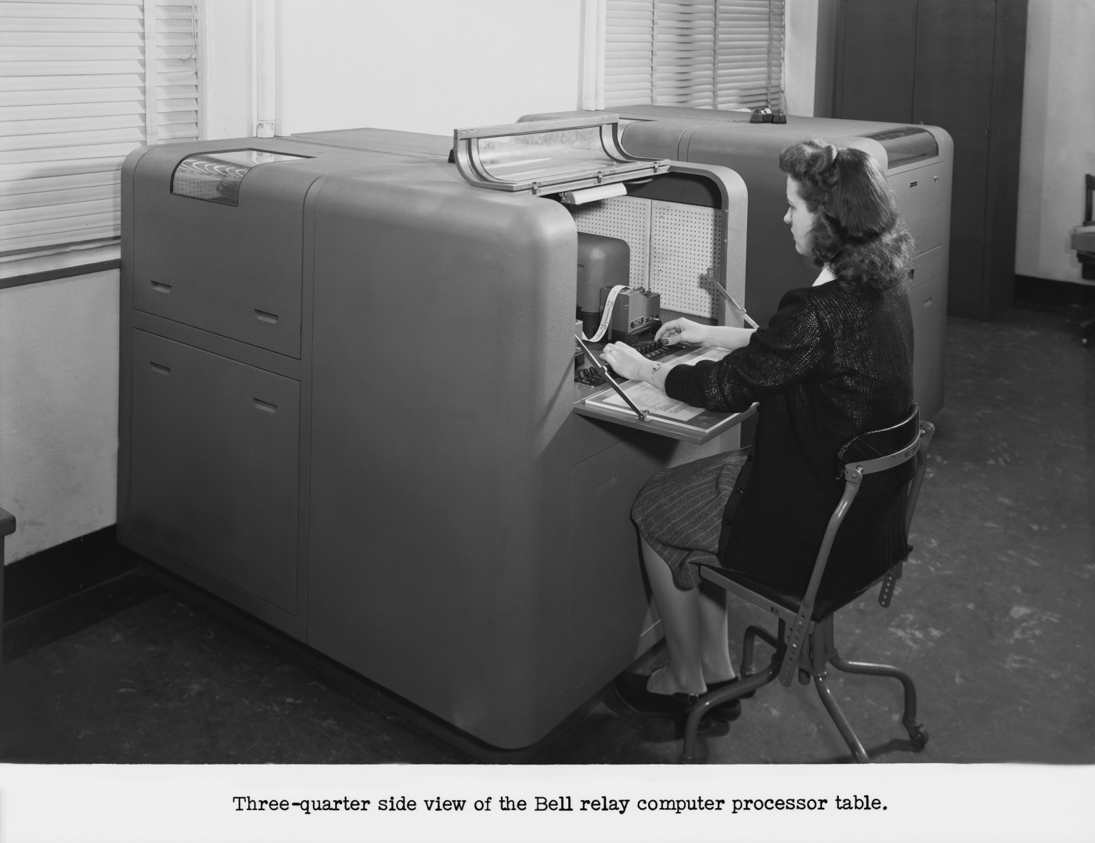 Woman seated in a chair working with a massive computing machine.