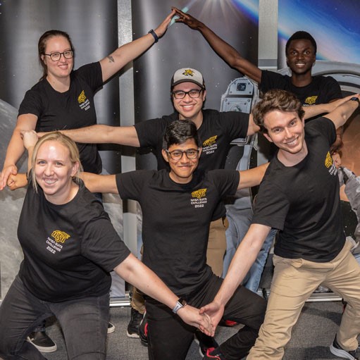 Group of people holding hands in a star formation and smiling for a group photo.