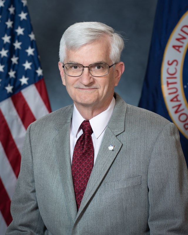 General David Stringer, with U.S. and NASA flags in background.