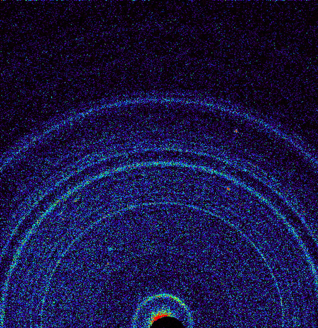 A scientific image. Tiny dots cluster against a black background. They form rings rippling from a black center, where there's a small cluster of red and yellow dots. 