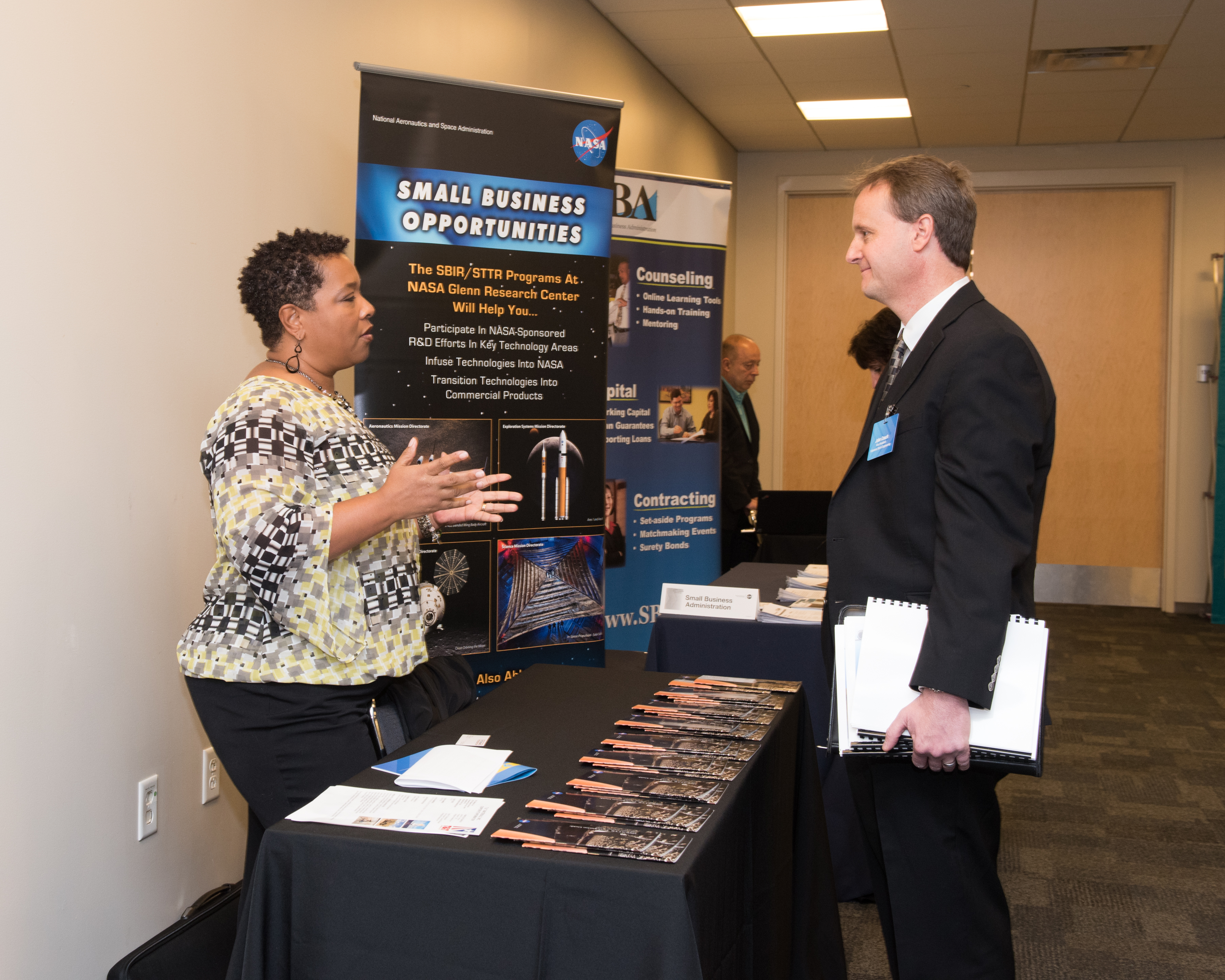 A business man speaks to a female NASA employee at a small business event.