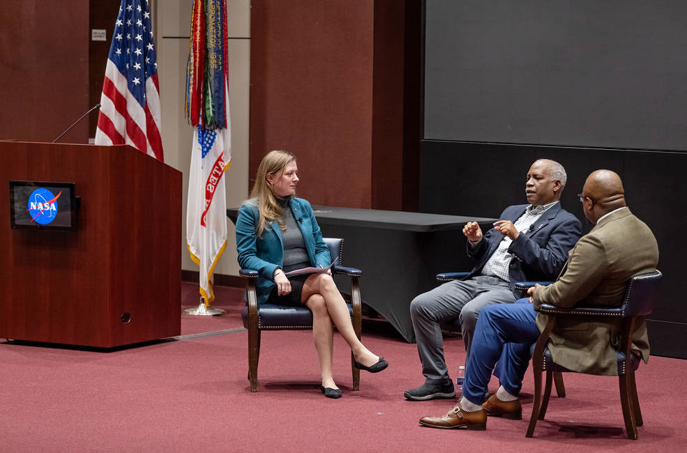 A woman is sitting in a chair on a stage chatting with two speakers at the MLK Jr. Day Event.