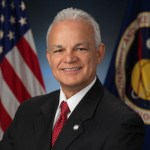 A white man with white hair and is in a suit poses for a picture in front of the American flag and the NASA flag