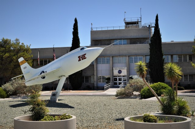 The X-1E rocket plane sits on a pedestal stand in front of the main entrance to an office building.