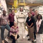 A group of eight people standing for a group photo. In the middle of the group is a person with an astronaut diving suit on.