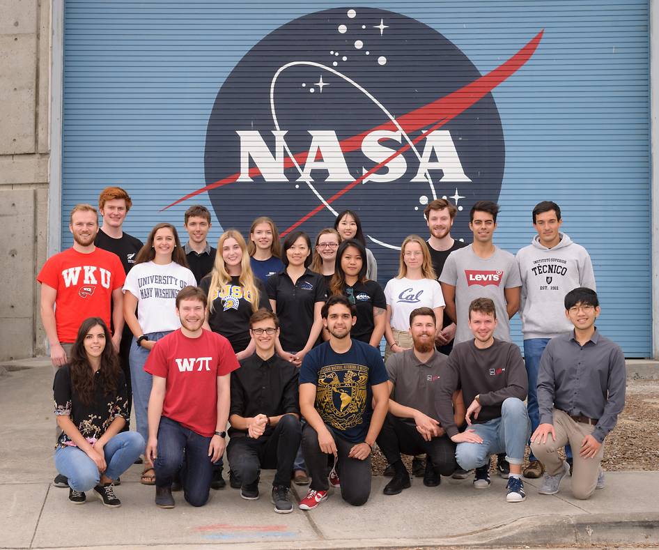Group of young people posing in front of a large NASA logo, smiling toward the camera.