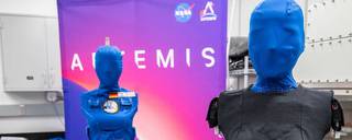 Two blue manikins stand in front of an Artemis sign. 
