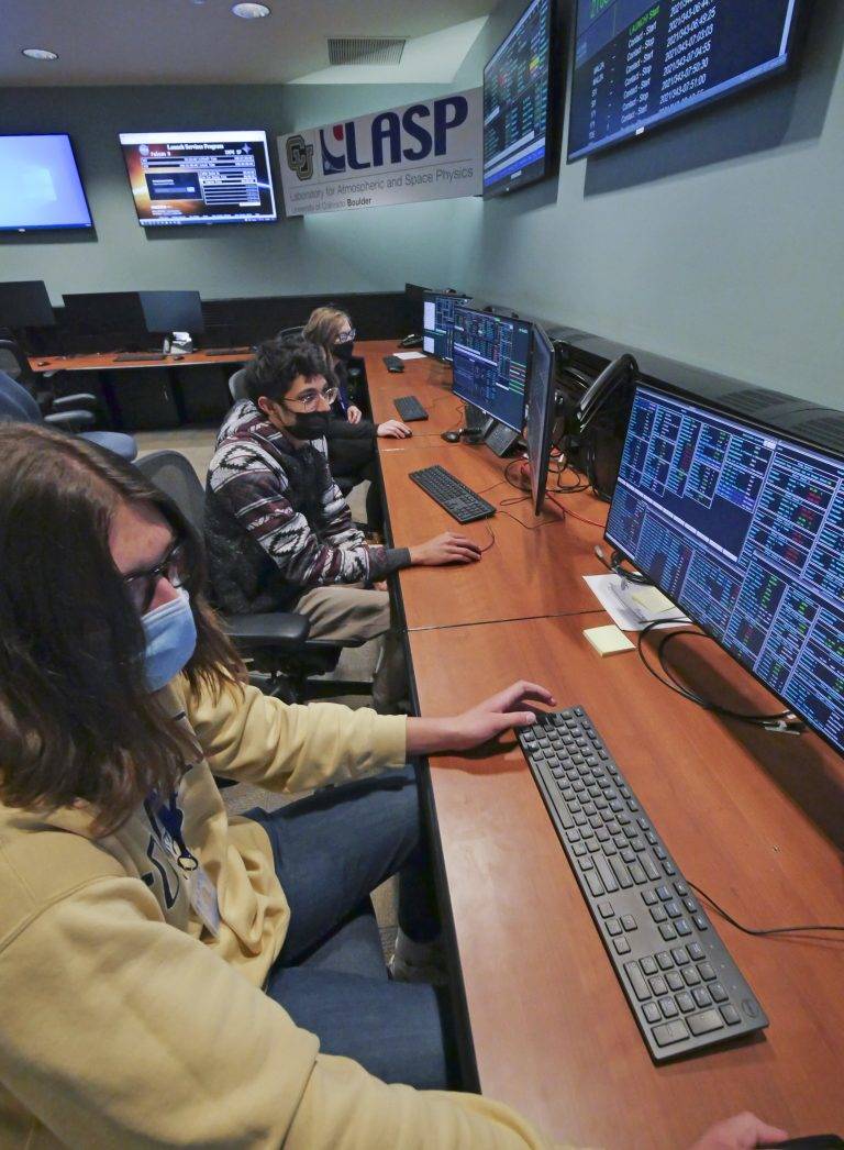 Students sit at a computer with masks on working on the LASP team for IXPE.