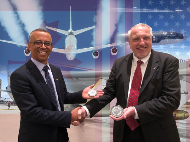 Two men representing Canada and the U.S. shake hands and exchange commemorative medallions celebrating their history of space and aeronautics research.