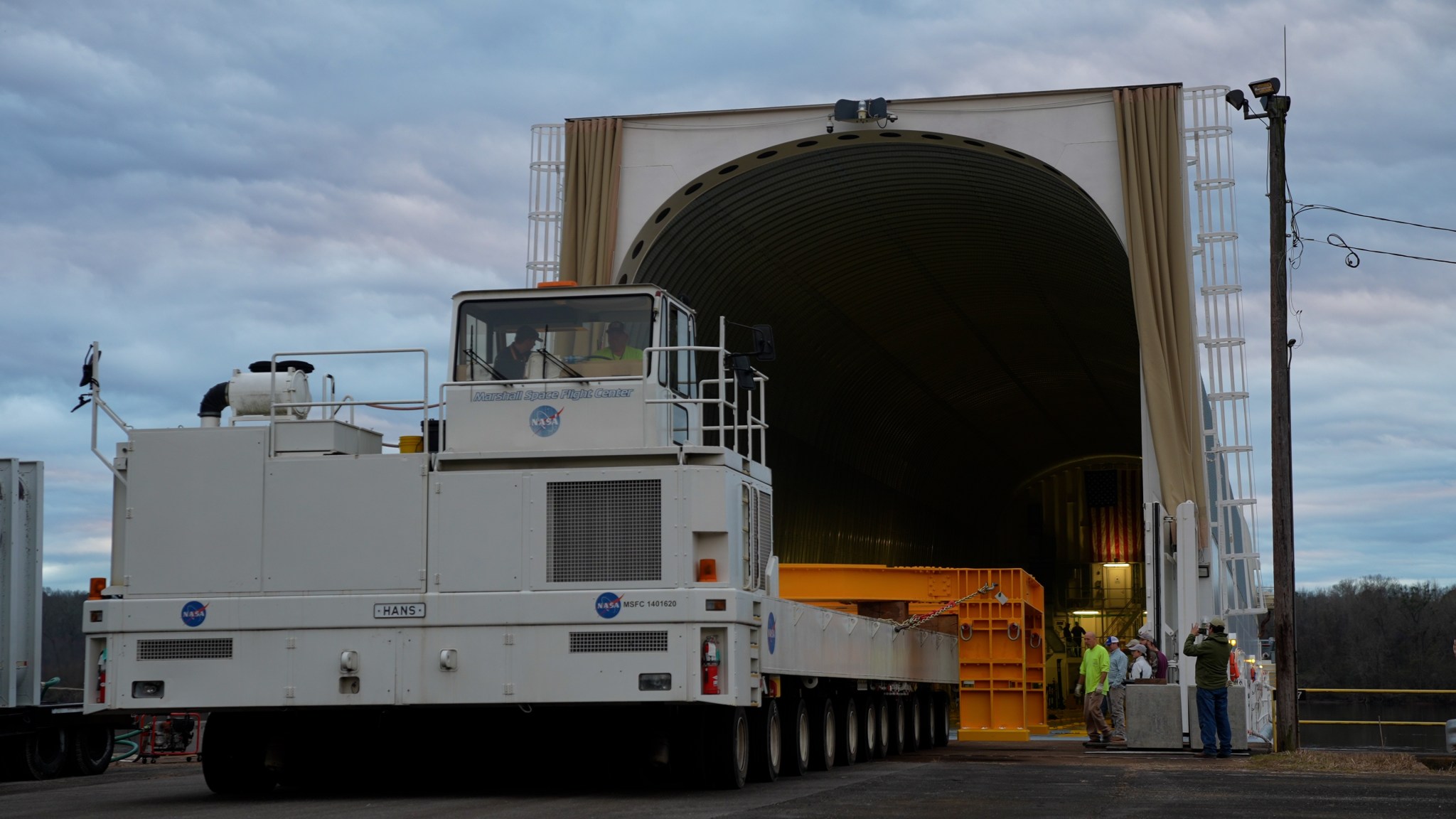 two workers sit in a large truck-like vehicle that is very large used to offload items from the hanger 