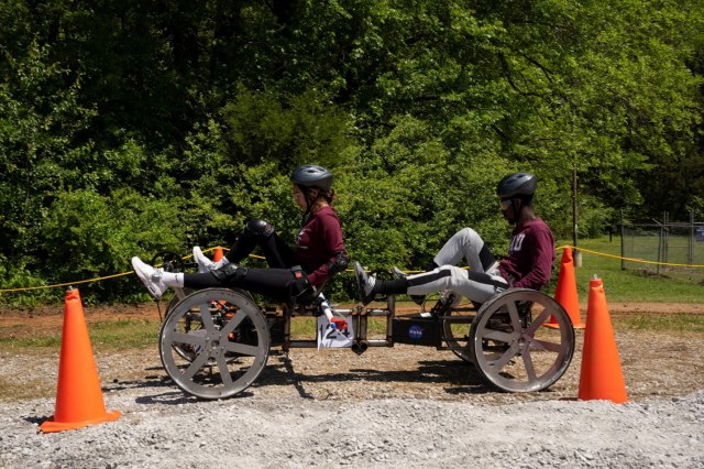 Two students travel over dirt terrain in man-made rover