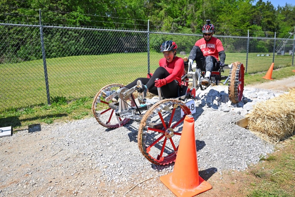 Two students travel over rocky terrain in man-made rover