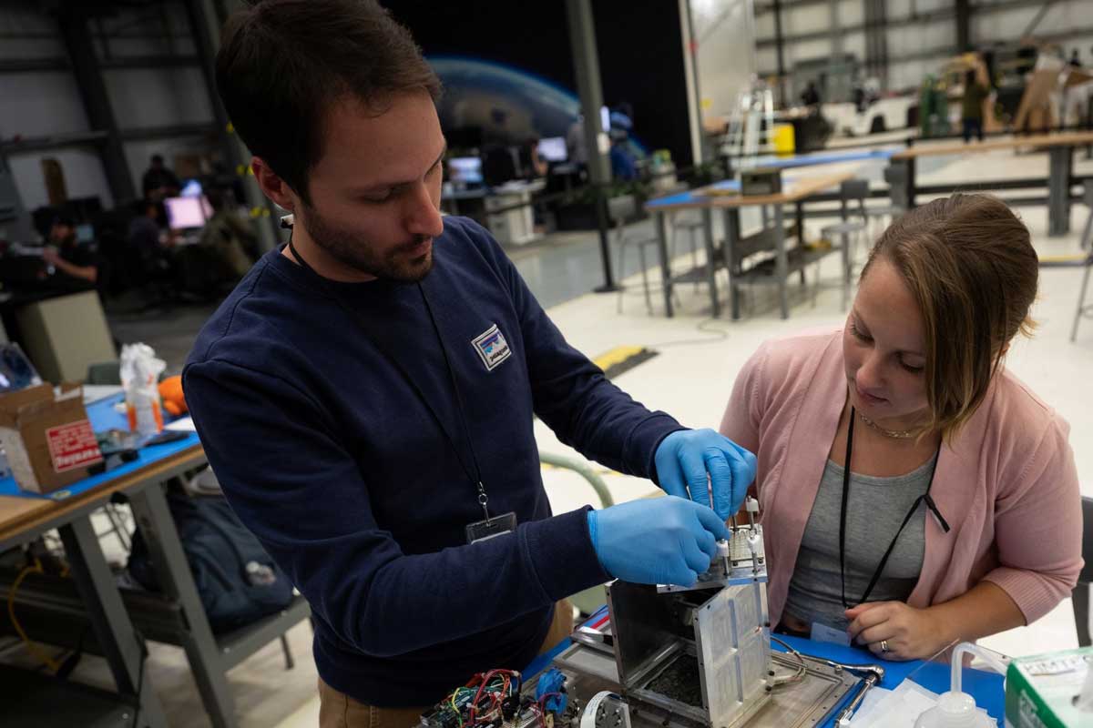 Two people work on a metal box.