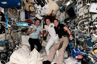 imagen de una astronauta de la NASA y dos cosmonautas posando para una foto en el interior de la estación espacial