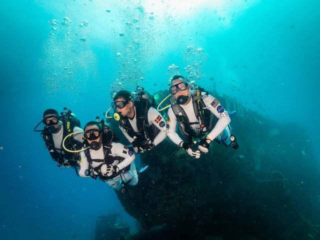 Aquanauts swimming in the ocean in front of a dark structure.