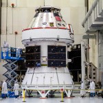 Technicians work on the Orion spacecraft with solar array wings exposed in the Operations and Checkout Building at Kennedy Space Center.