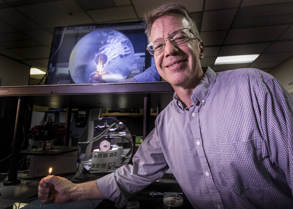 Tom Moss, software team lead in the Applied Physics Laboratory, demonstrates the Schlieren effect with a lighter on Dec. 12, 2018. Schlieren systems are used to display changes in the air not visible to the naked eye. Here, hot air rises off the flame, and the image is reflected by the mirror below and displayed on the screen above.