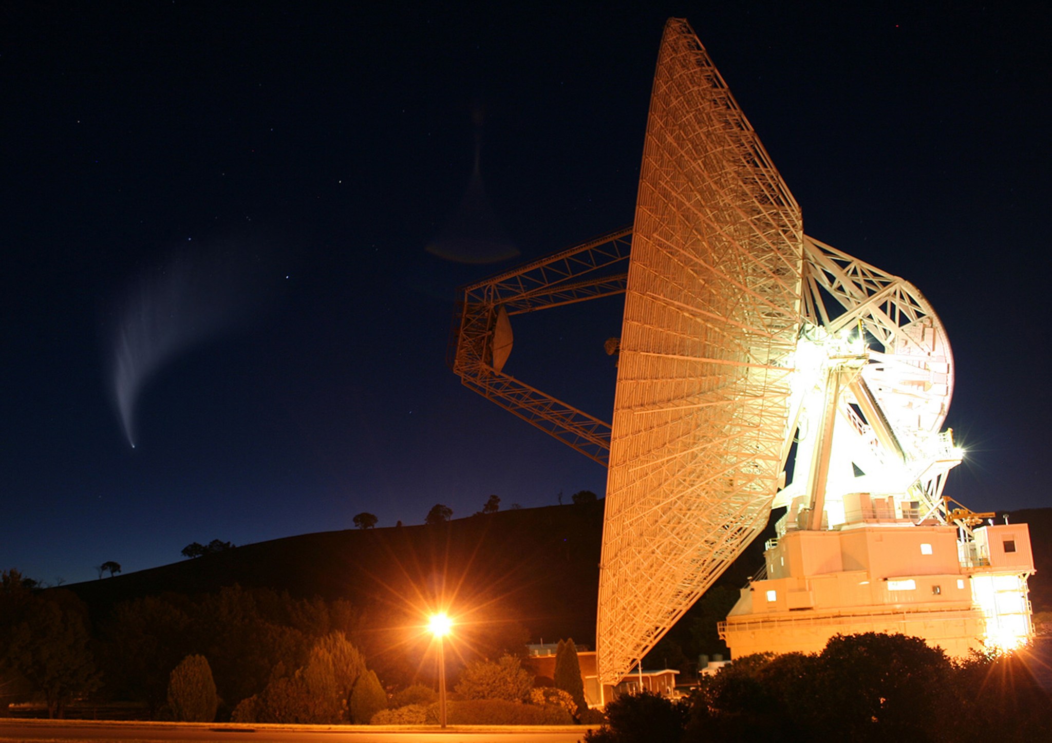 A massive antenna lights up the surrounding starry night sky with golden hues.