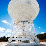 A white antenna stretches across the photo, backlit by the Sun on a bright blue sky.