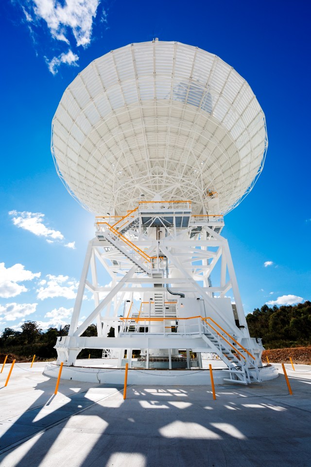 A white antenna stretches across the photo, backlit by the Sun on a bright blue sky.