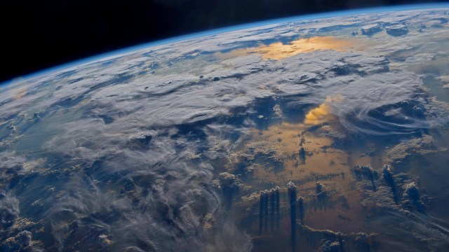 ISS photo of Eath's limb, showing clouds over the sea and sunset glint on the waters below.