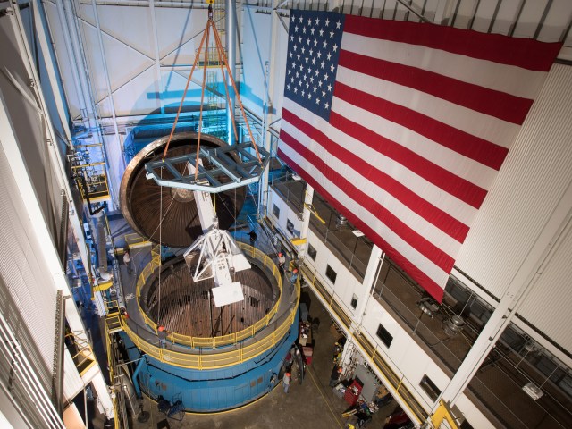 Overhead view of open vacuum chamber with hardware attached to overhead crane.