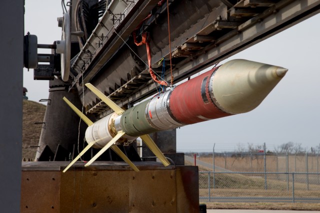 A sounding rocket attached to a launcher. The rocket, from bottom to top, has yellow fins on the bottom, a white body section, bright yellow fins, a dark green section, a silver body section then a red body section, and then a silver cone-shaped top.
