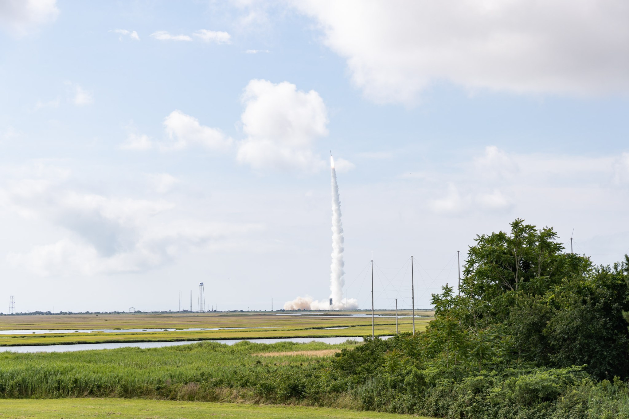 A rocket launches in the distance with a plume of white smoke trailing underneath.