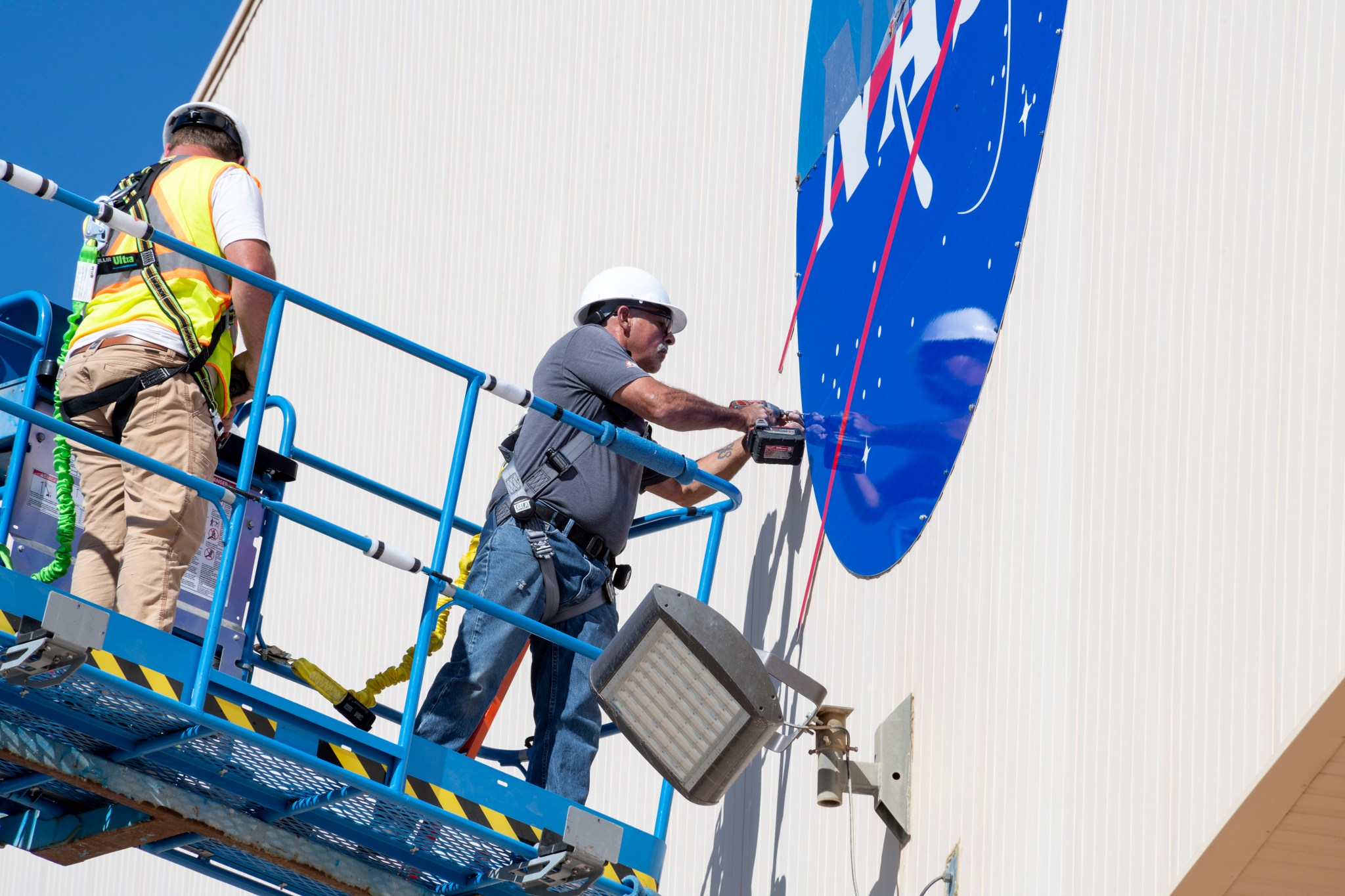 Two workers replace the NASA meatball sign on the side of a building.