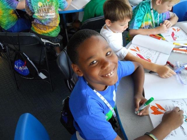 Male ASTRO CAMP goer looks up while coloring and smiles