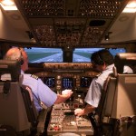 Photo of the Boeing 747 cab of the CVSRF. Two pilots are seated in the cockpit and are adjusting the controls between them.