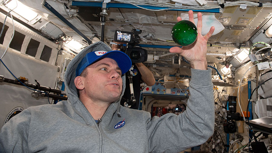 Astronaut Josh Cassada plays with a sphere of water flying in microgravity dyed with green food coloring and bubbling due to an antacid that was placed inside.