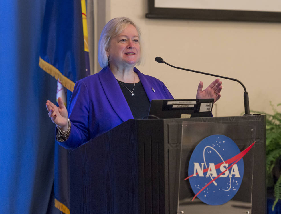 A woman wearing a royal blue blazer speaks at a podium bearing the NASA logo