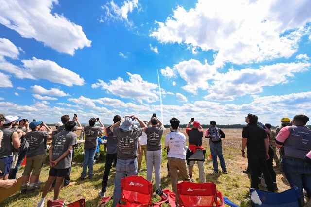 A small crowd watches as a rocket launches.