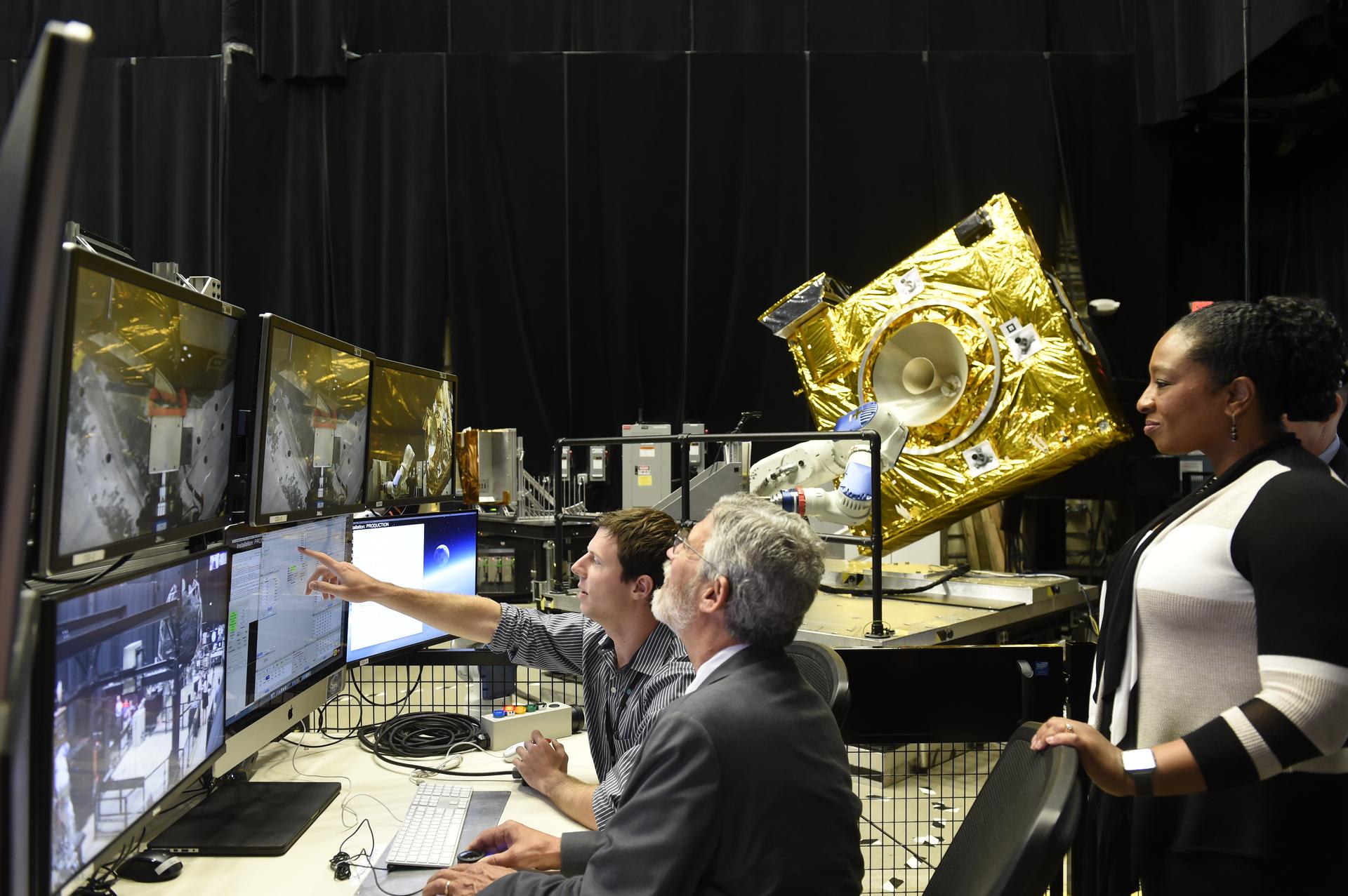 Dr. Holdren (center) operates a robotic arm within the Robotic Operations Center as roboticist describes the ROC’s simulation capabilities, and Deputy Center Director for Technology and Research Investments at Goddard observes the demonstration.