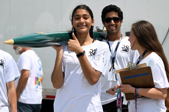 Student gives thumbs up while helping teammate carry rocket.