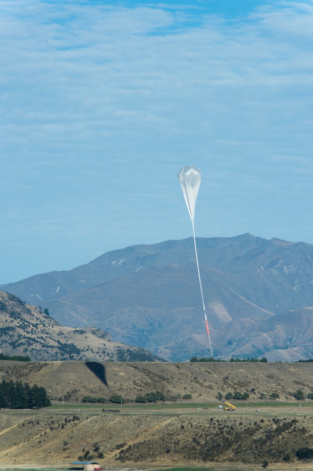 A landscape photo of New Zealand, with a partially inflated balloon in the shape of an upside down teardrop in the distance.