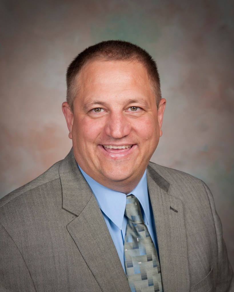 Portrait of a man dressed in a suit and tie and who is smiling.